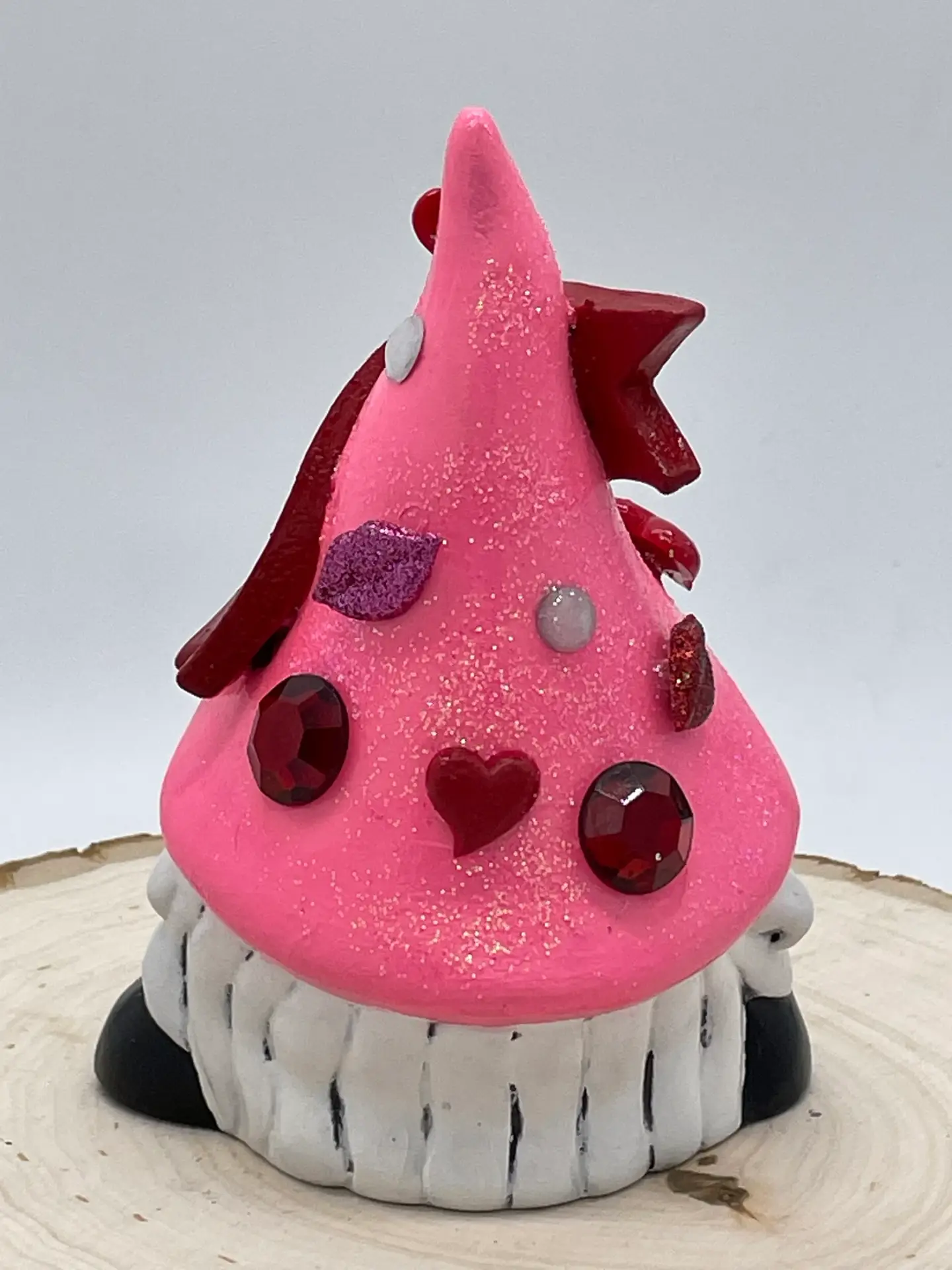 Birthday Gnome for February wearing pink hat with heart and lip shaped gems, and a dark red banner across that reads February in White, Right Back.